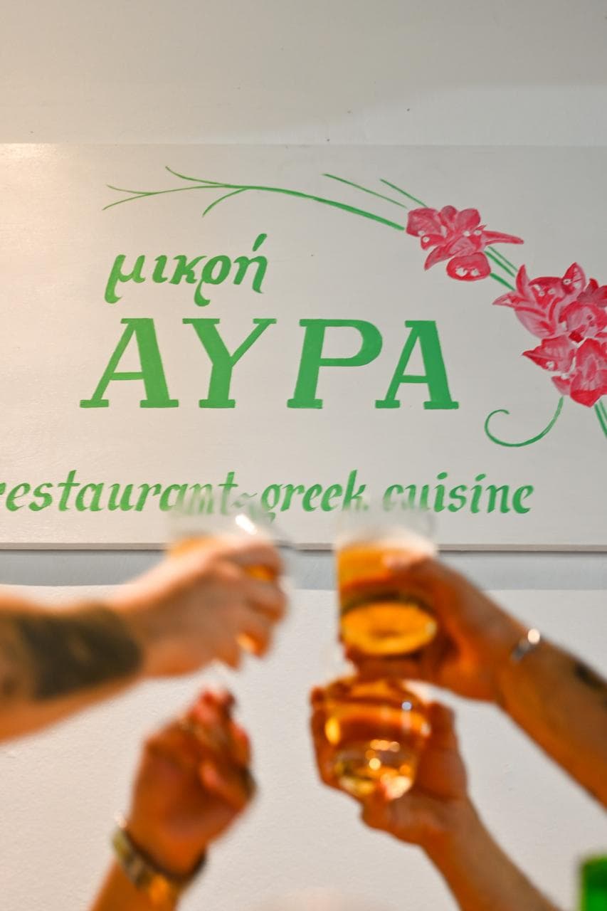 A toast raised in front of the painted Mikri Avra sign.